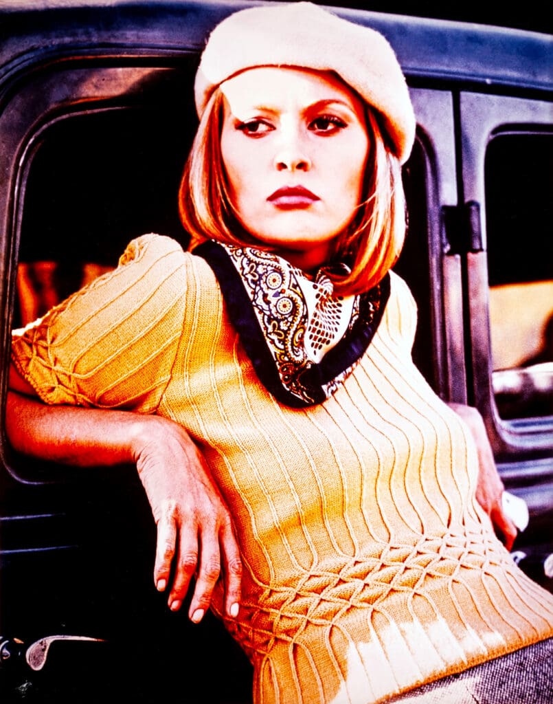 A woman in yellow sweater and had leans against a car