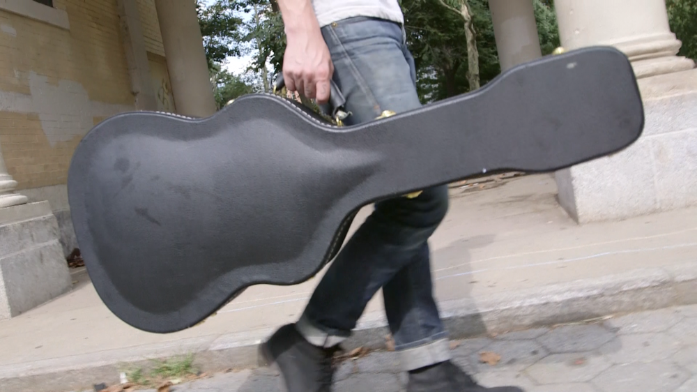 Picture of someone holding a guitar case, most likely with a guitar in it