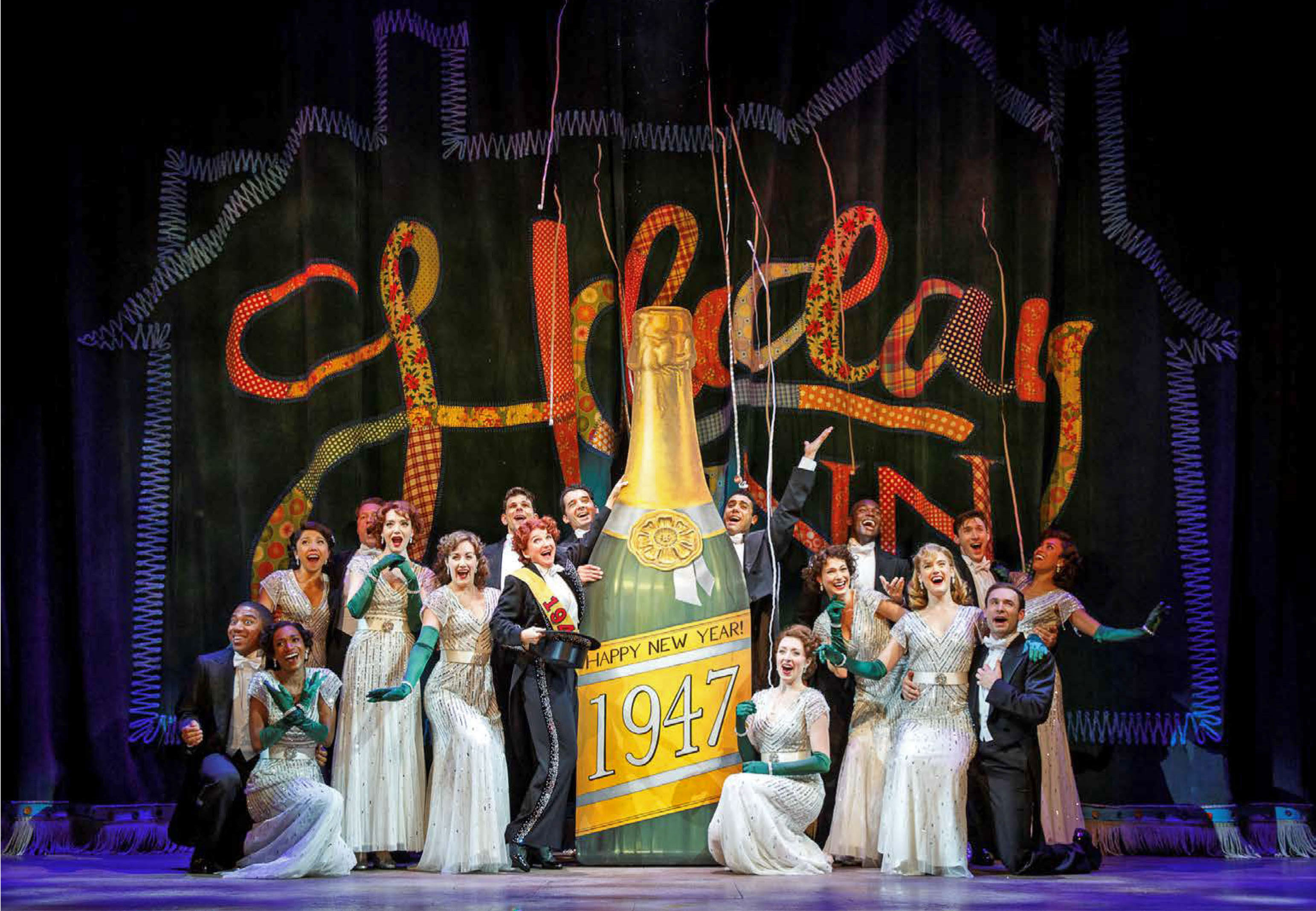 cast on stage with giant champagne bottle that reads 1947