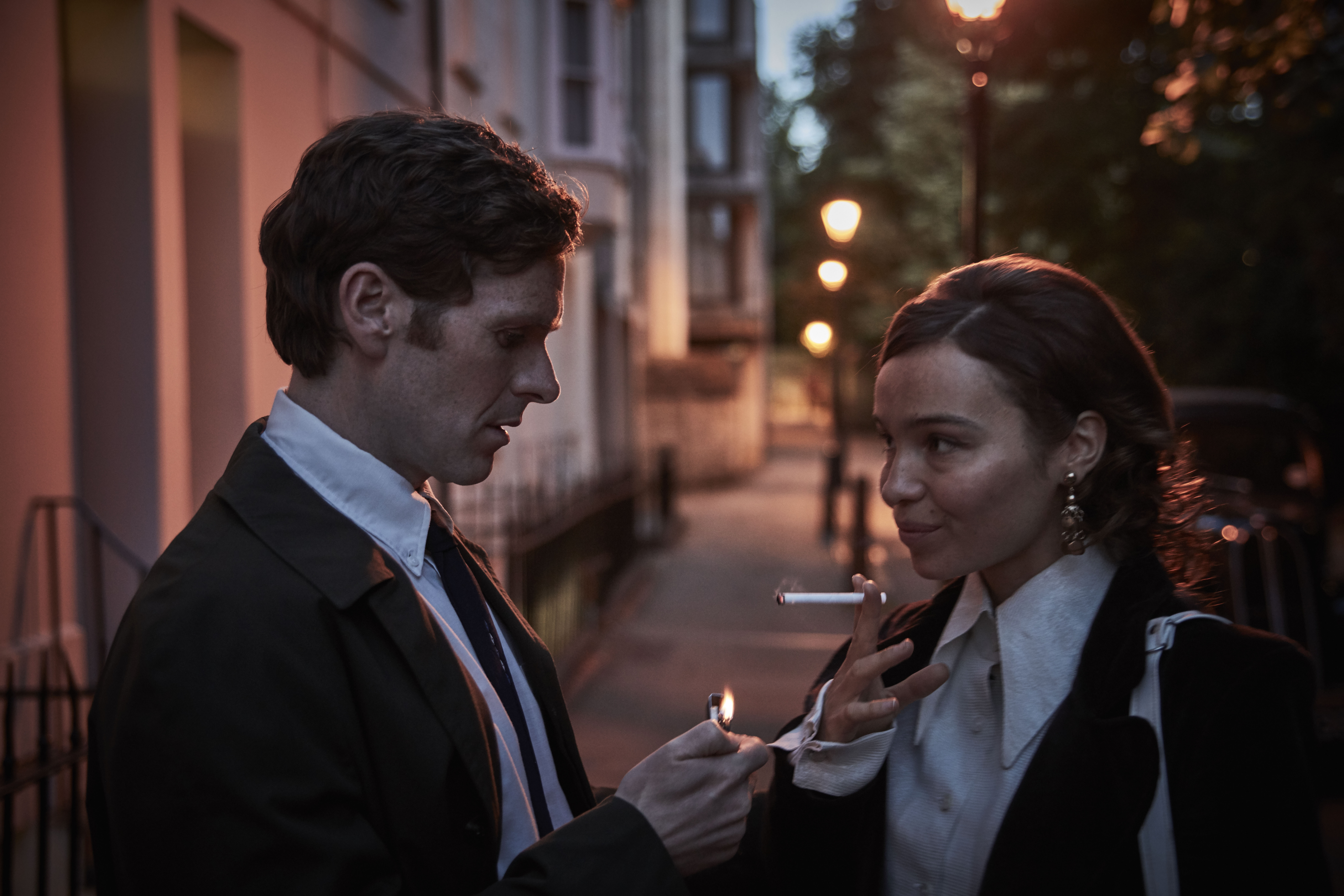 man helping smiling woman light cigarette standing on British street