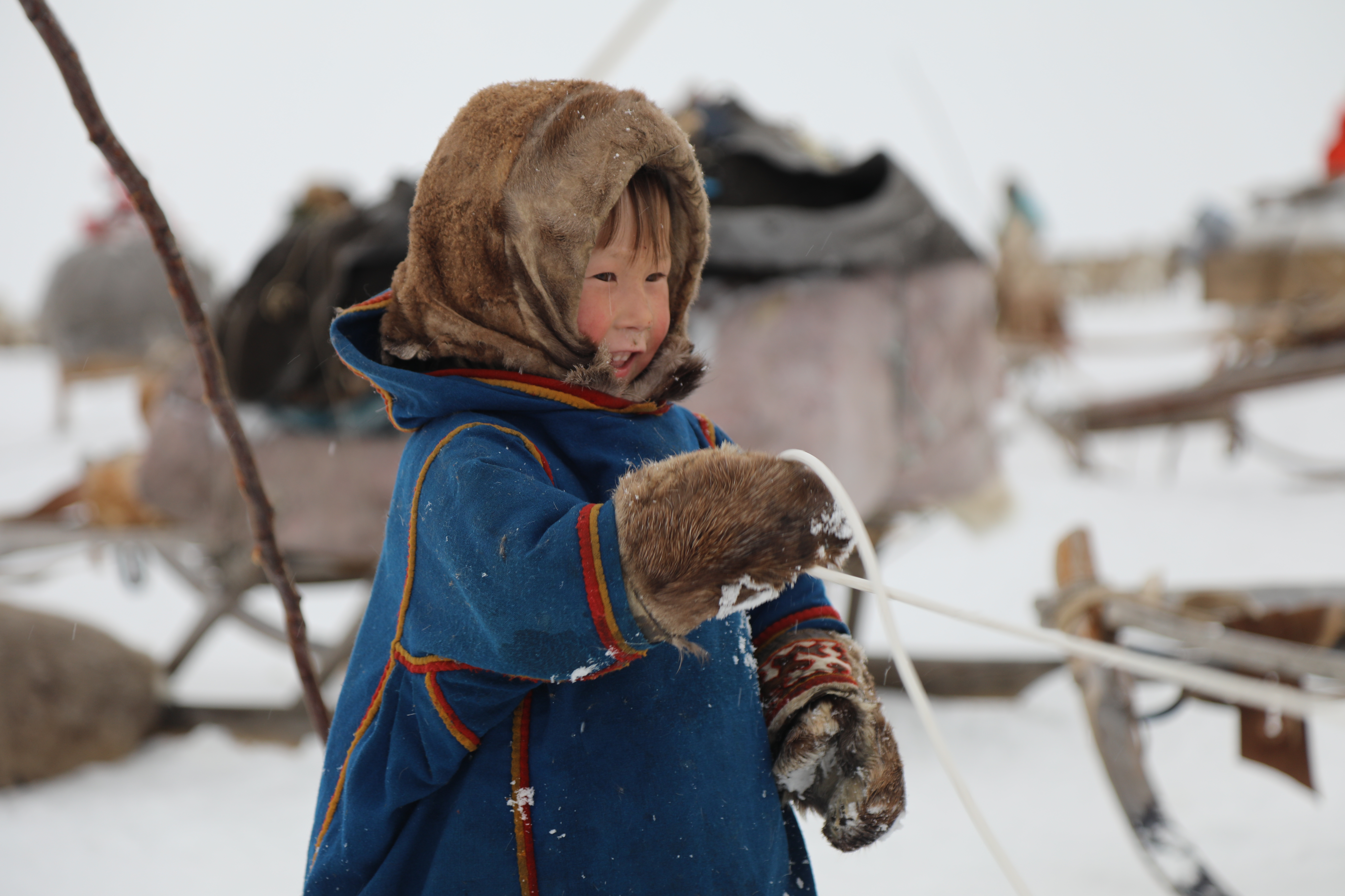 child wearing eskimo gear standing in the snow holding a rope