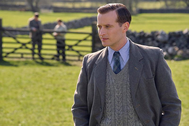 sharp young man in a suit, sweater vest, tie standing in grass image