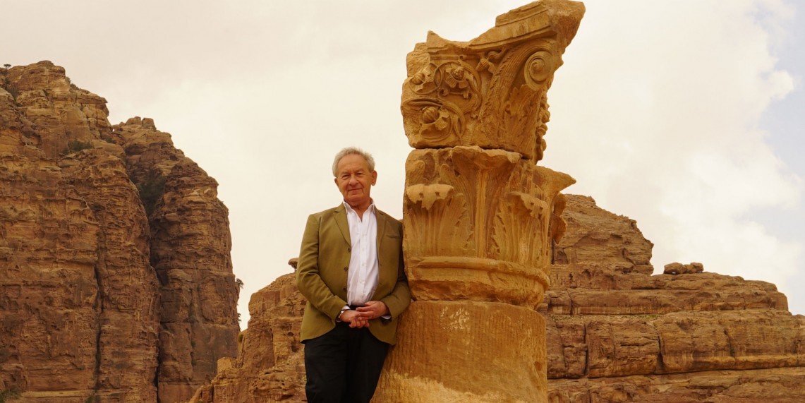 host standing in front of ancient carved column and mountains