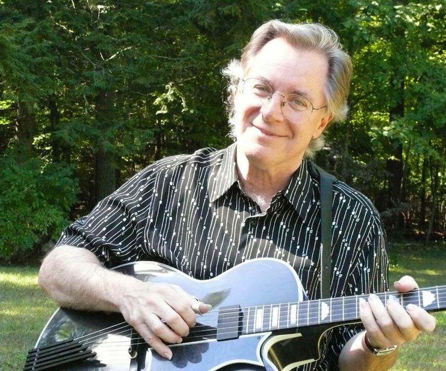 john sebastian playing a black guitar outdoors