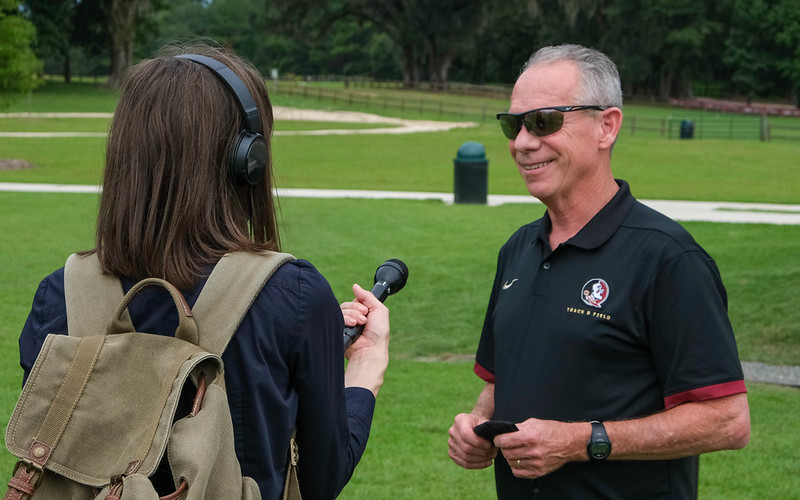 female reporter holds out microphone to interview man in FSU sport shirt