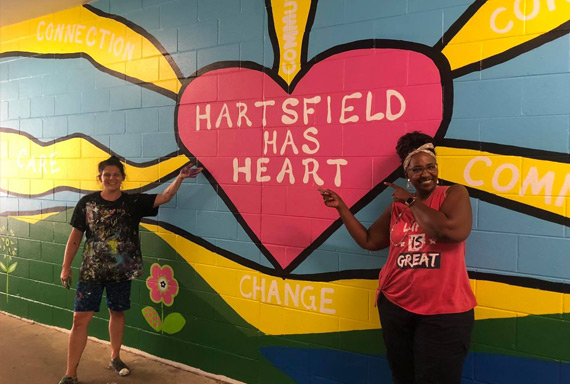 Hartsield Elementary mural and two teachers posing in front of it