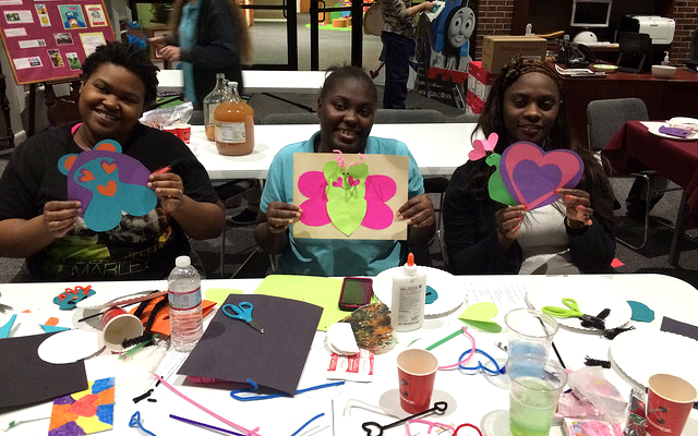 3 teachers holding up artwork at a table full of crafting materials