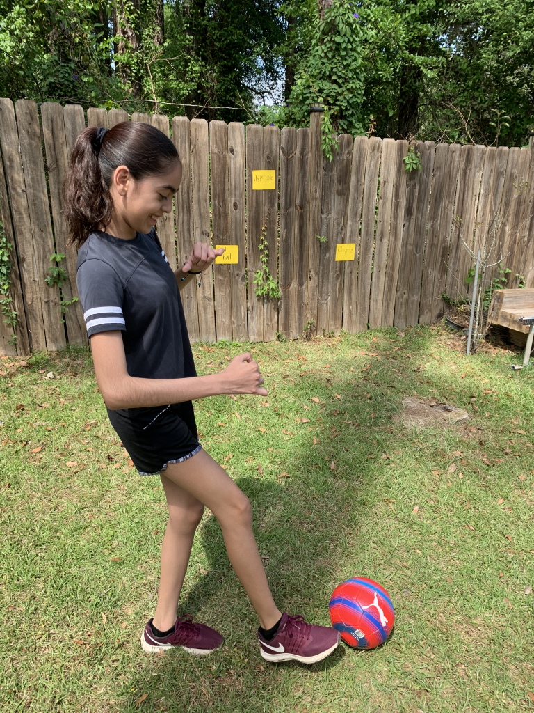 girl kicking a red and blue soccer ball to a fence with sticky notes 