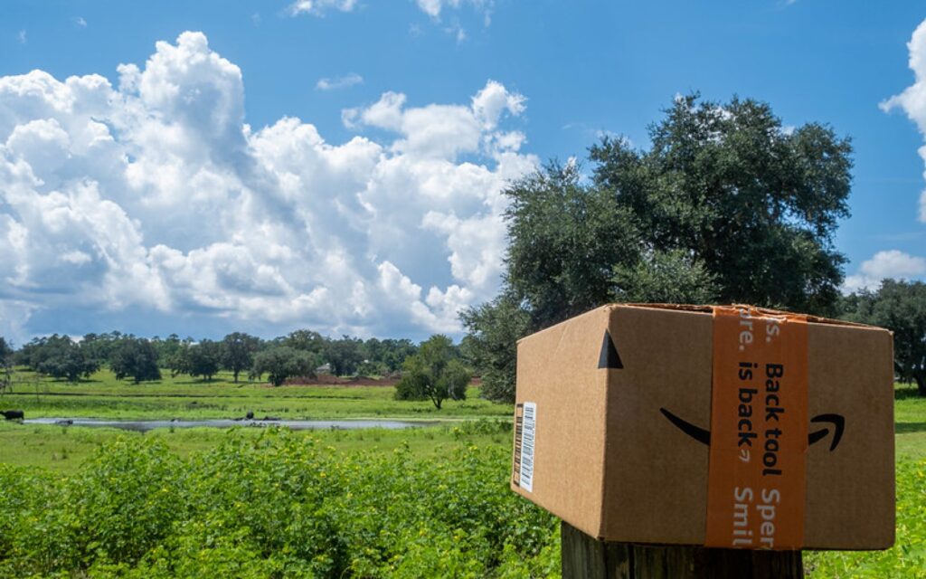 An amazon package sits atop a wooden post overlooking a lush green field.