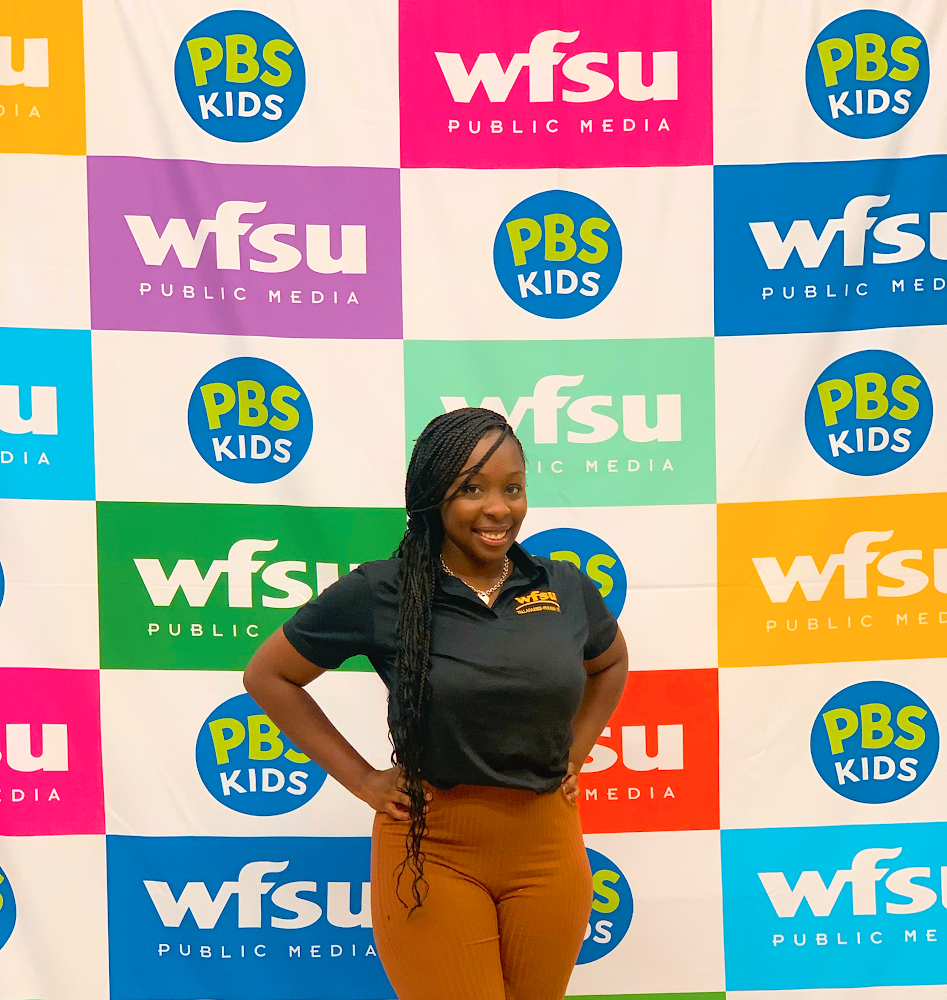 woman in black shirt standing in front of wfsu step and repeat background