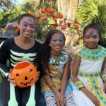 a woman and two girls dressed in halloween costumes sitting on a bench