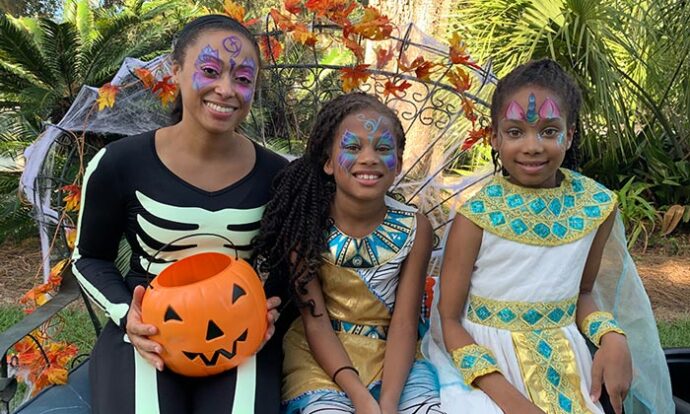 a woman and two girls dressed in halloween costumes sitting on a bench