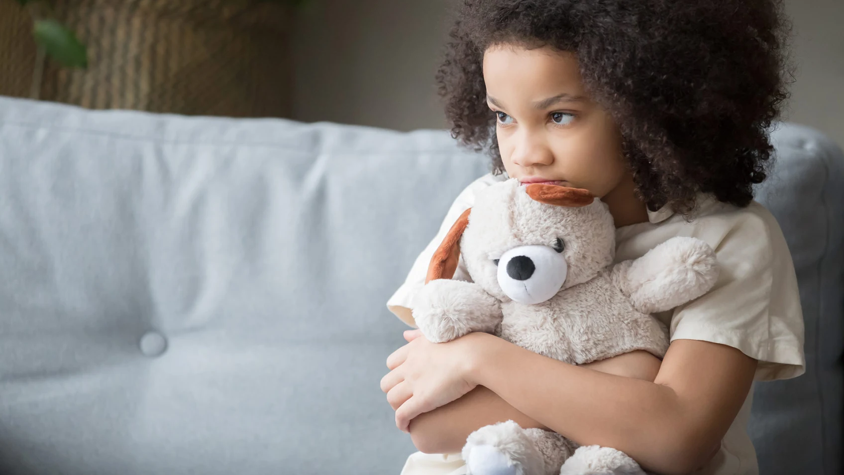 Young child hugging a teddy bear stuffed animal while looking off to the side sad.