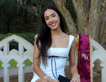 Gaby is pictured in a white dress sitting on a white bench with a garnet and gold FSU graduation stole.