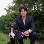 Kai Smith squats in a black suit on the grass in front of a push along with his dog.