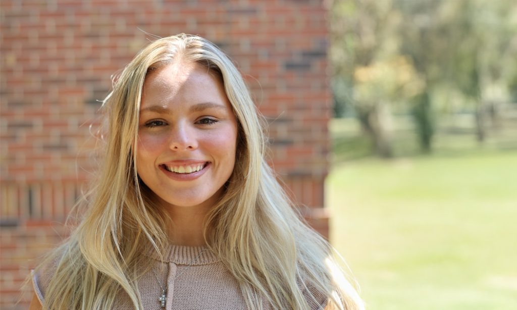 A smiling woman stands in front o a red brick wall.