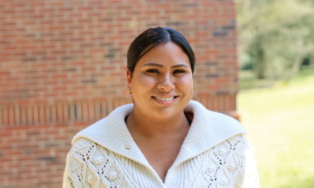 A smiling woman stands in front of a brick wall