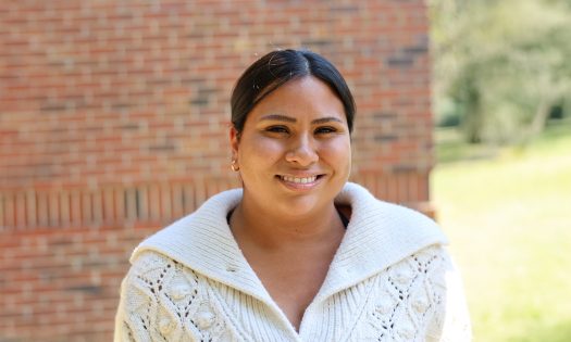 A smiling woman stands in front of a brick wall