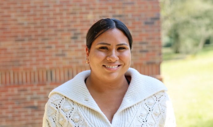A smiling woman stands in front of a brick wall