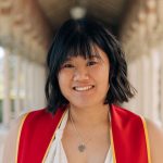 A smiling woman in red stands in front of white columns.