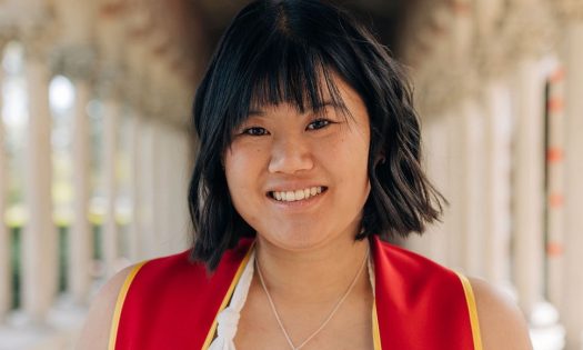 A smiling woman in red stands in front of white columns.