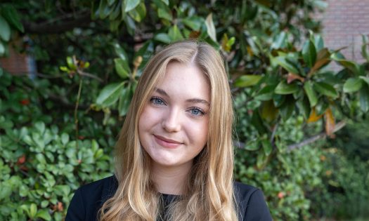 A smiling woman dressed in black stands in front of shrubbery.