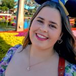 A smiling woman stands in front of color flowers beneath a monorail
