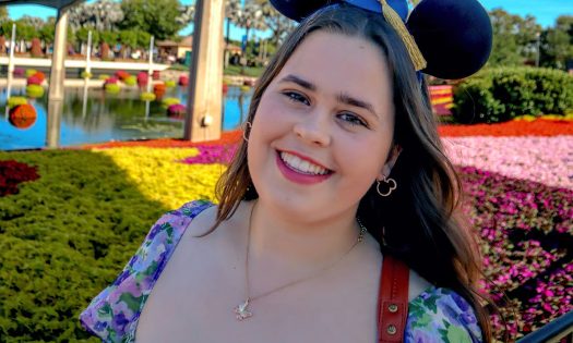 A smiling woman stands in front of color flowers beneath a monorail