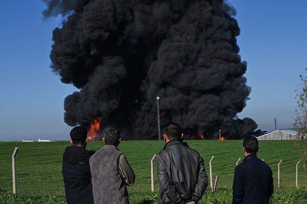 People watch as smoke billows from an oil warehouse in the Kani Qirzhala area on the outskirts of Erbil, the capital of Iraq