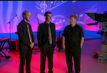 The Men and Music of the World Music Trio Three musicians stand on stage in pink and blue lit up room