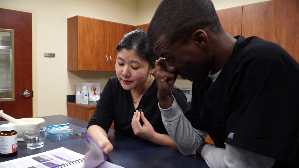 Two people in black medical scrubs looking at a book at a table.