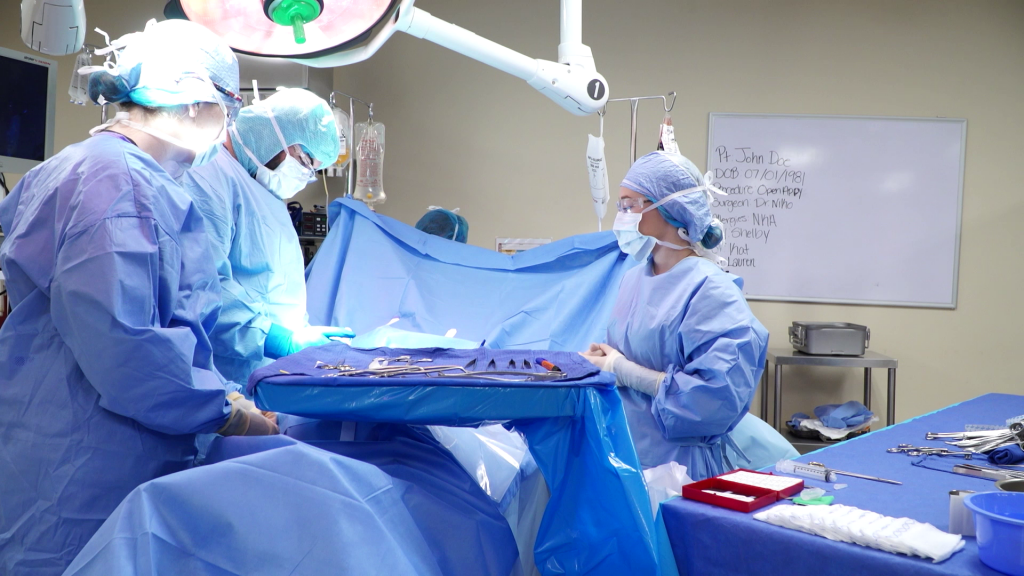 Three people in medical scrubs standing over an operating table.