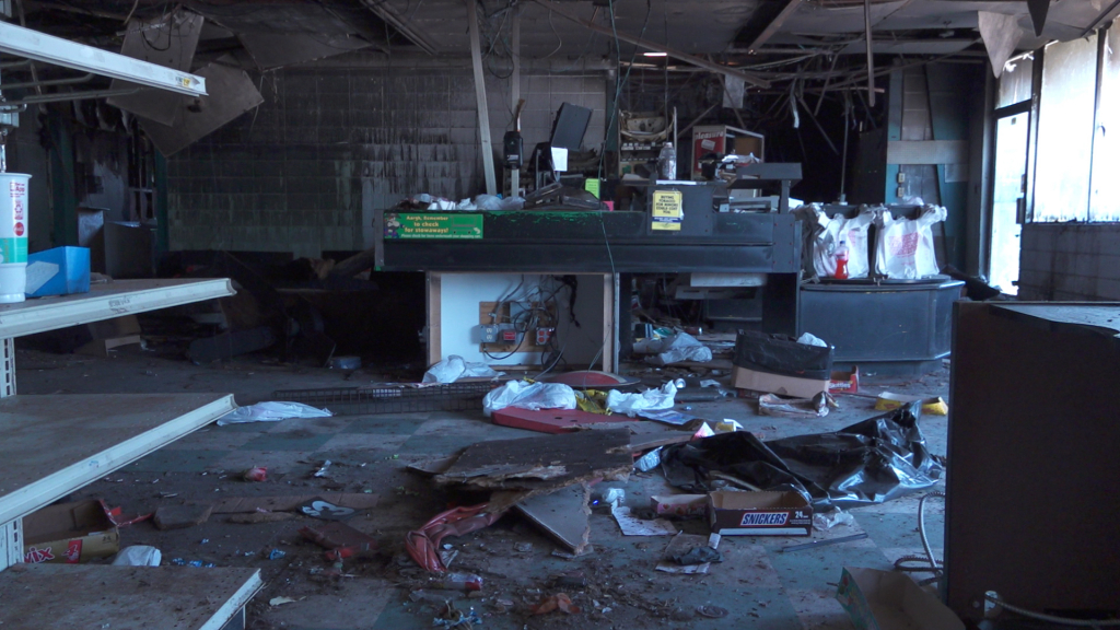 Empty and burned shelves and counters in a store. The roof is also damaged.