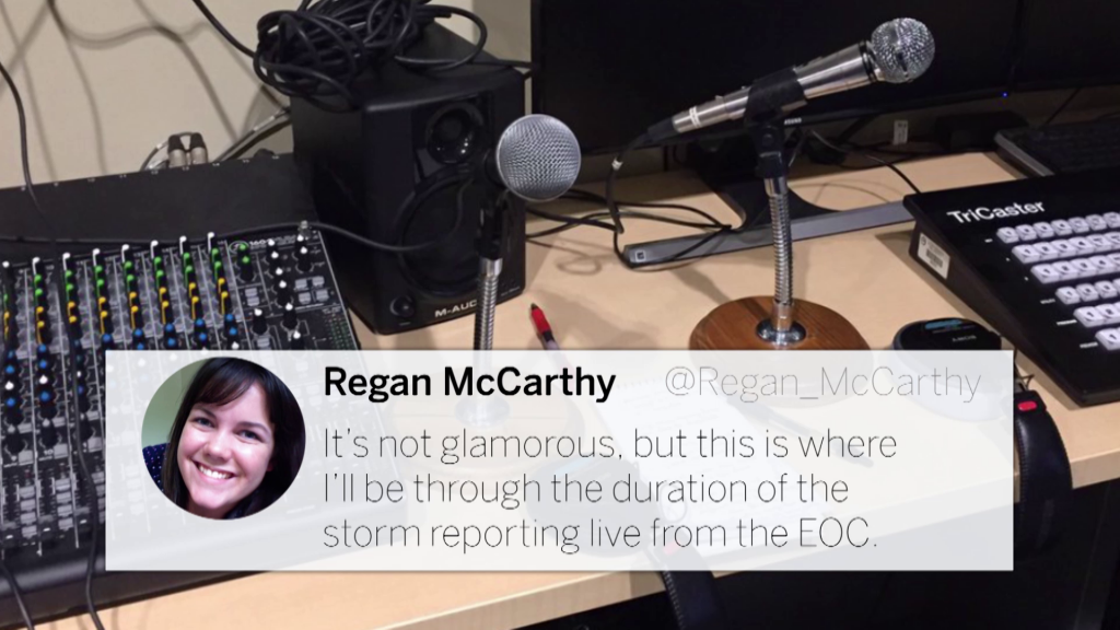 A desk with a computer  and microphones on a table with a quote that says" It's not glamorous, but this is here I'll be through the duration of the storm reporting live from the EOC."