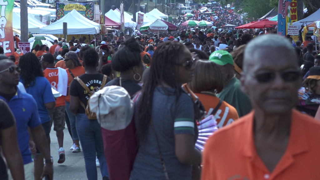 A large crowd of people gathered at an outdoor event with tents.