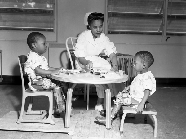 A nursing sitting at  little table with two children with braces on their legs.