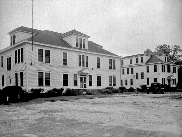 A vintage photo of  two white wooden buildings that appear to be connected.