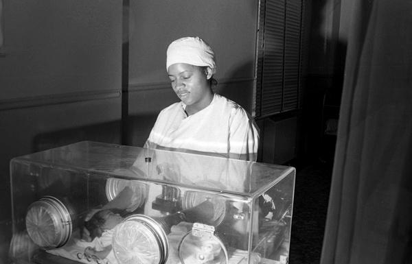 Local Routes: Retro Local (Episode 503) A person standing next to baby in incubator at hospital.,