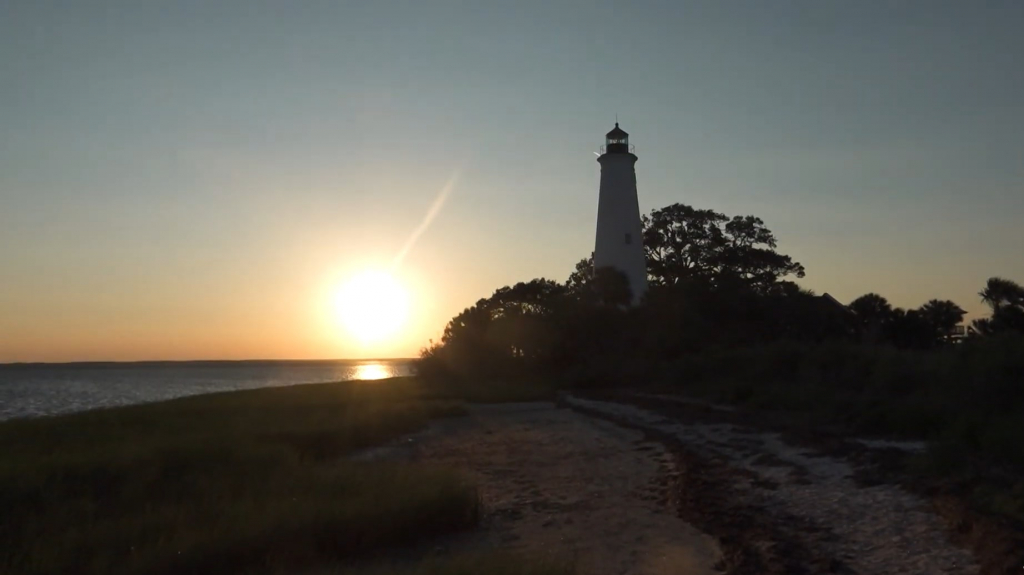 A sunset over a the Apalachee  Bay with the white tower of a lighthouse in the foreground.