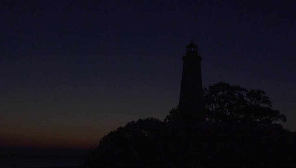 Silhouette of a lighthouse against the darkened sky moments after the sun dips behind the horizon.  There is a pinprick of light coming from the lamp room of the lighthouse