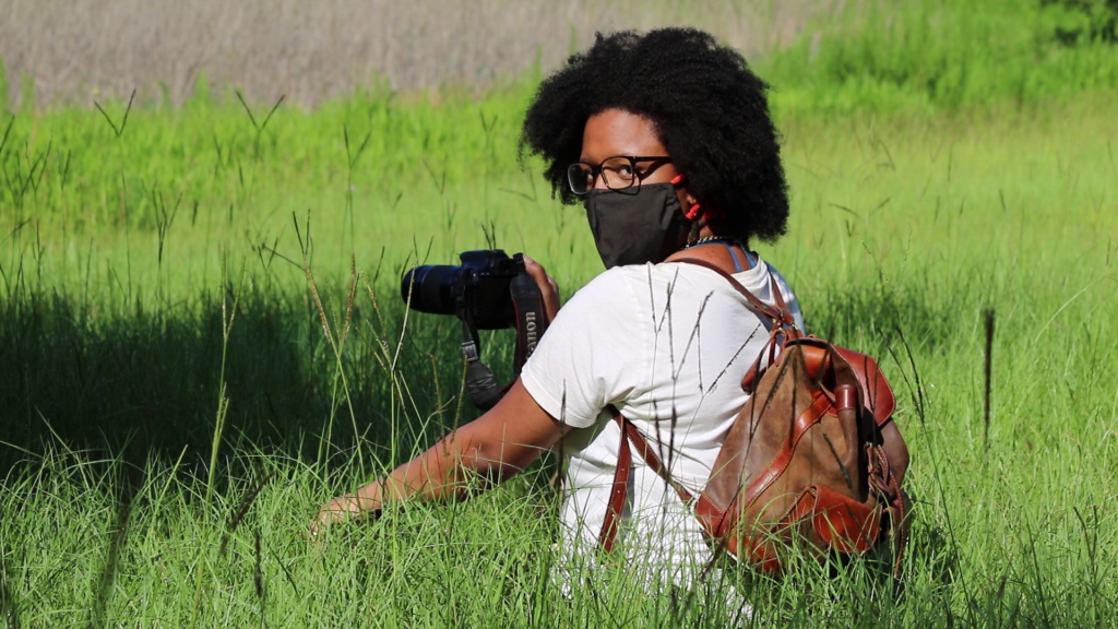 A woman in a green field with camera .