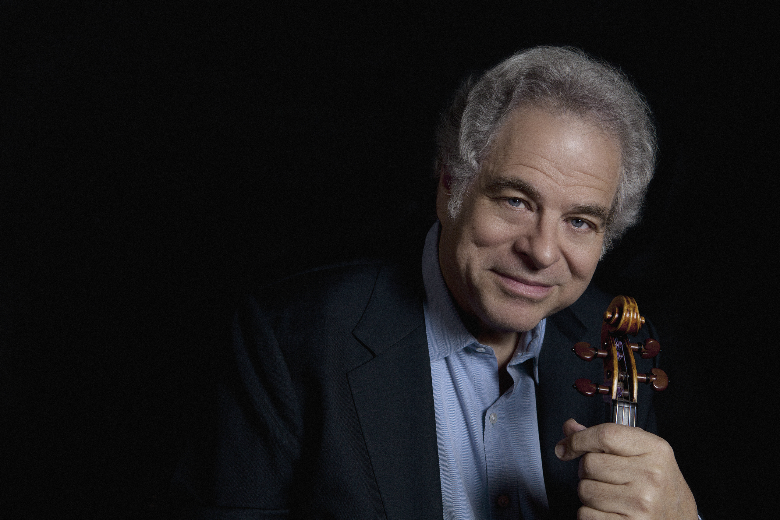 Itzhak Perlman wearing a suit and tie holding a cell phone