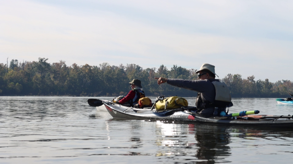 A man pointing while riding on a kayak in the water.