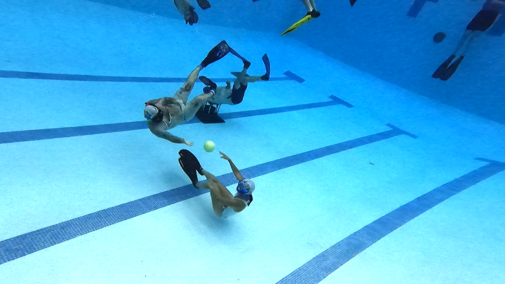 People passing a ball while swimming underwater.