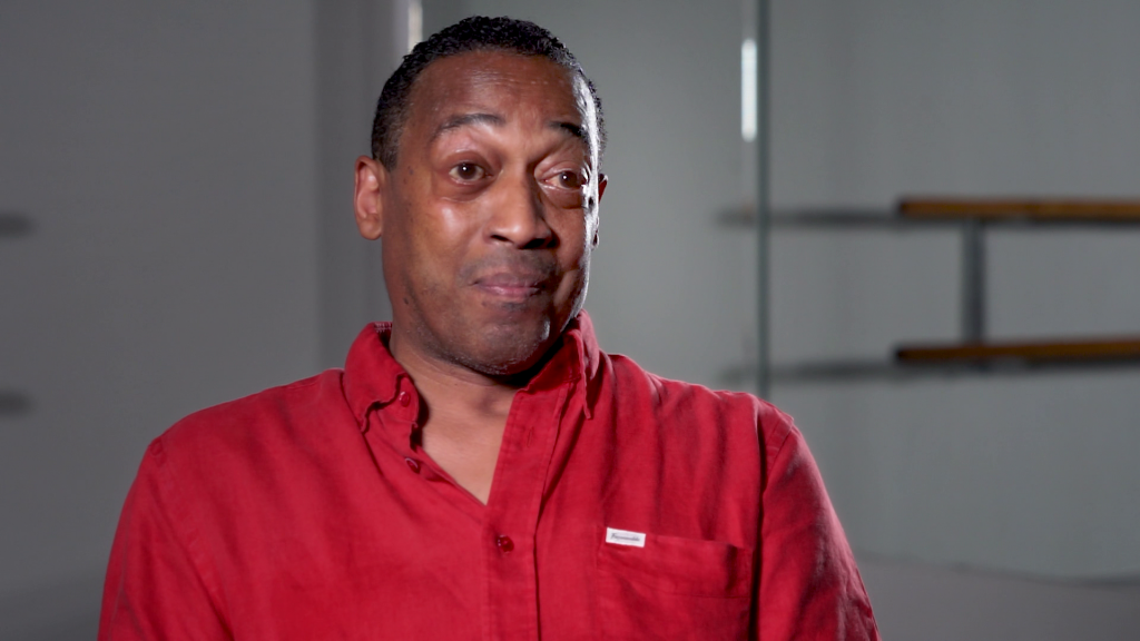 A man in red shirt looking at the camera during interview.