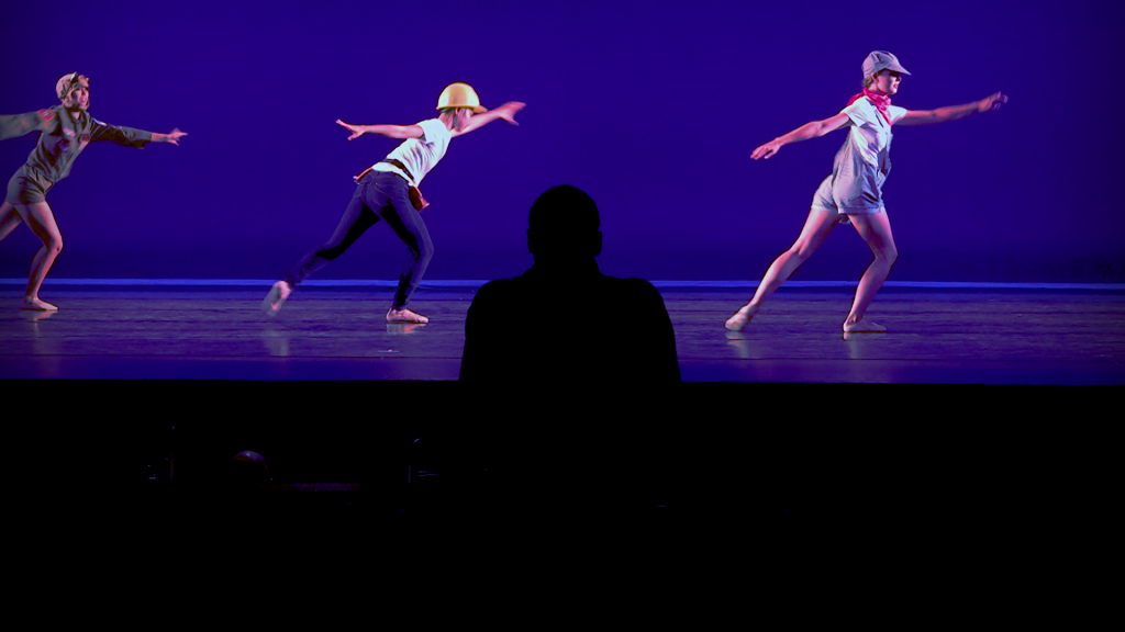 three on stage dancing , A person's silhouette watching them perform.