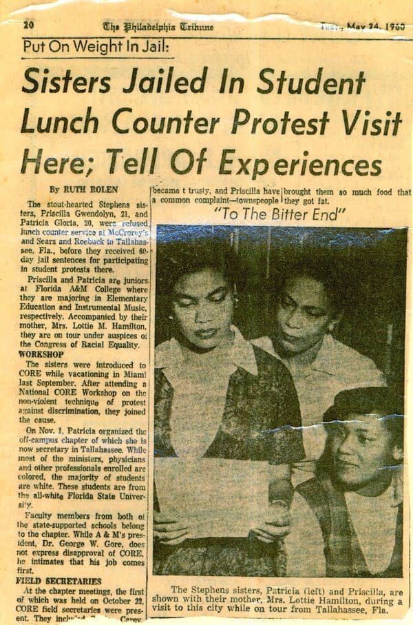 A close-up of a newspaper article from the Philadelphia Tribune on May 24, 1960. The headline reads "Sisters Jailed in Student Lunch Counter Protest Visit Here; Tell of Experiences." Included is a photo of two young women and their mother reading a piece of paper.