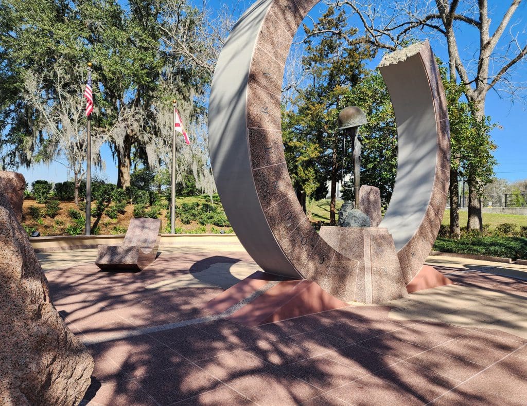 A sculpture of broken circle with helmet resting on rifle at center