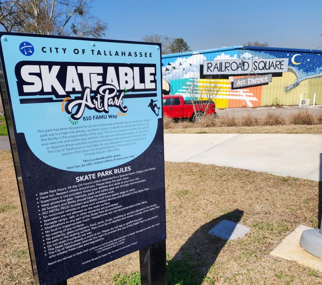 Sign describing rules of teh sakteable art park and a mural on the side of a building declaring the area the Railroad Square Art District