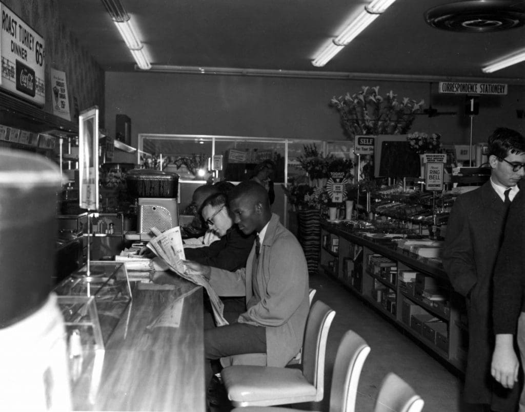 A black man and a white man sitting at lunch counter in a restaurant